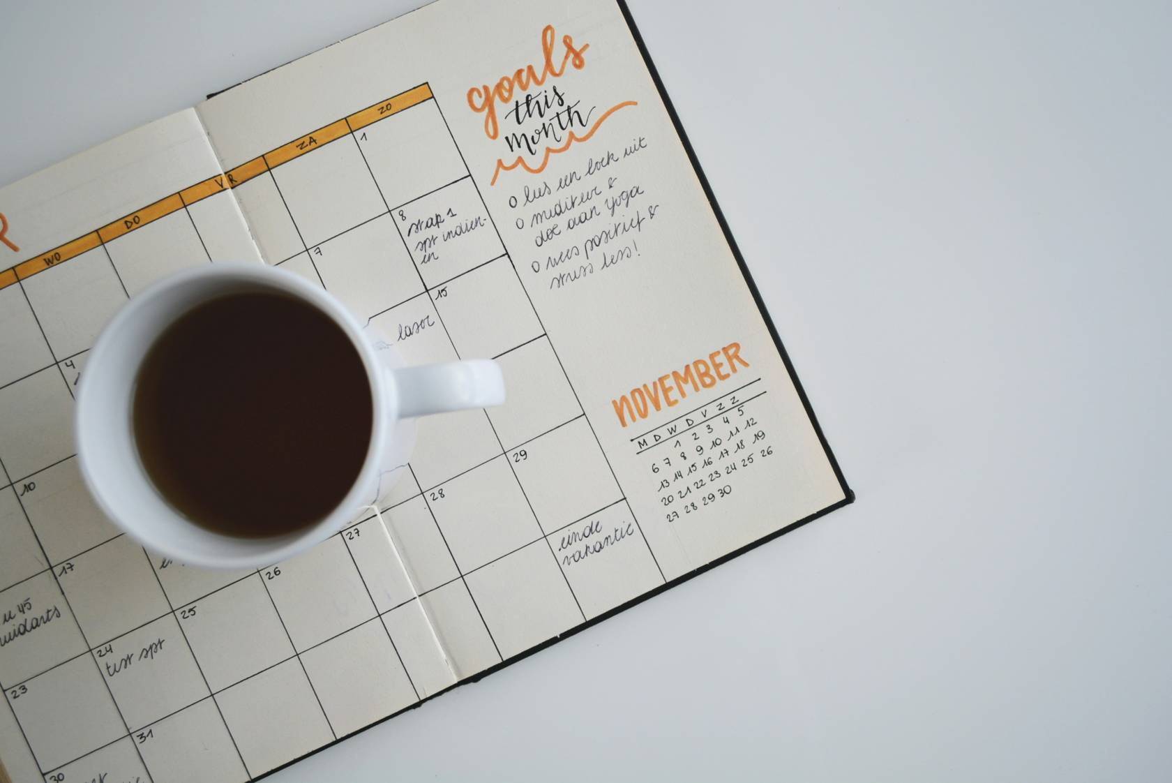 A calendar with text and numbers, office supplies scattered around, a coffee cup, and a teacup on a table.
